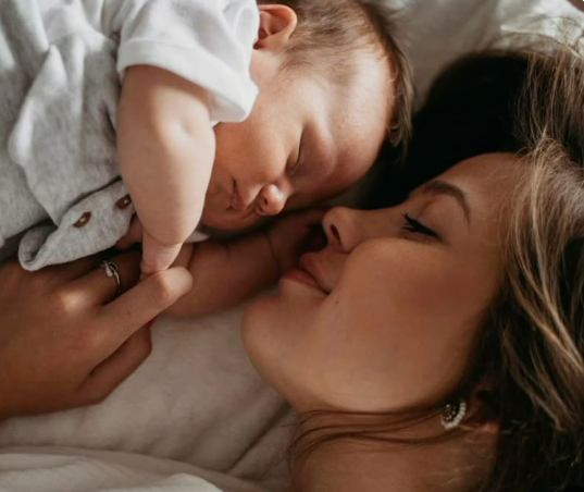 Jeune mère allongée contre son bébé endormi, partageant un moment tendre de proximité et de calme.