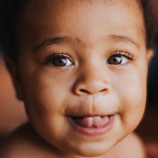 Tendresse en regard Gros plan d’un bébé souriant avec la langue entre les lèvres et un regard pétillant.