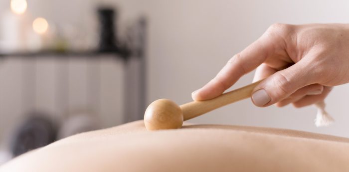 Massage doux au bâton de madérothérapie pour une détente profonde Main utilisant un petit bâton de madérothérapie en bois pour masser délicatement la peau d'une personne.